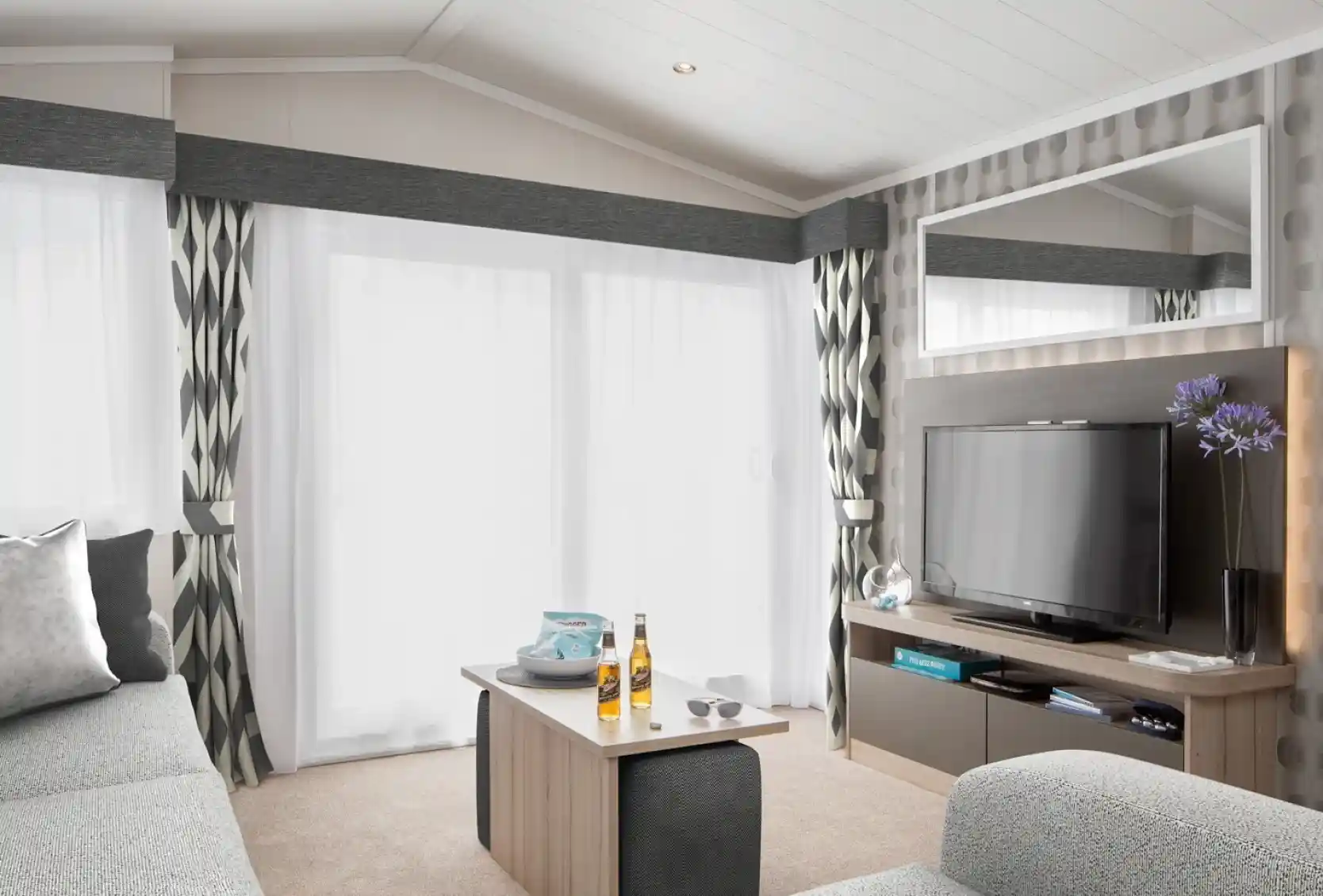 Modern living room with grey sectional sofa, coffee table with drinks, and TV entertainment centre.