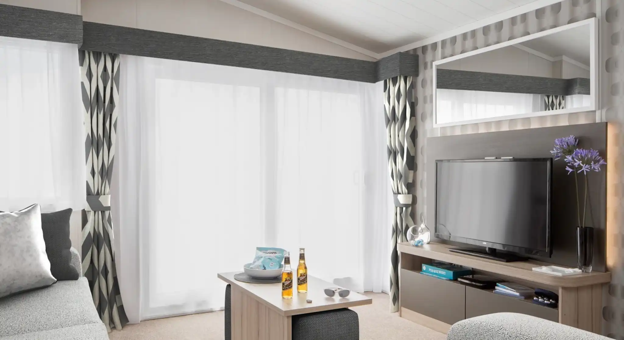 Modern living room with grey sectional sofa, coffee table with drinks, and TV entertainment centre.