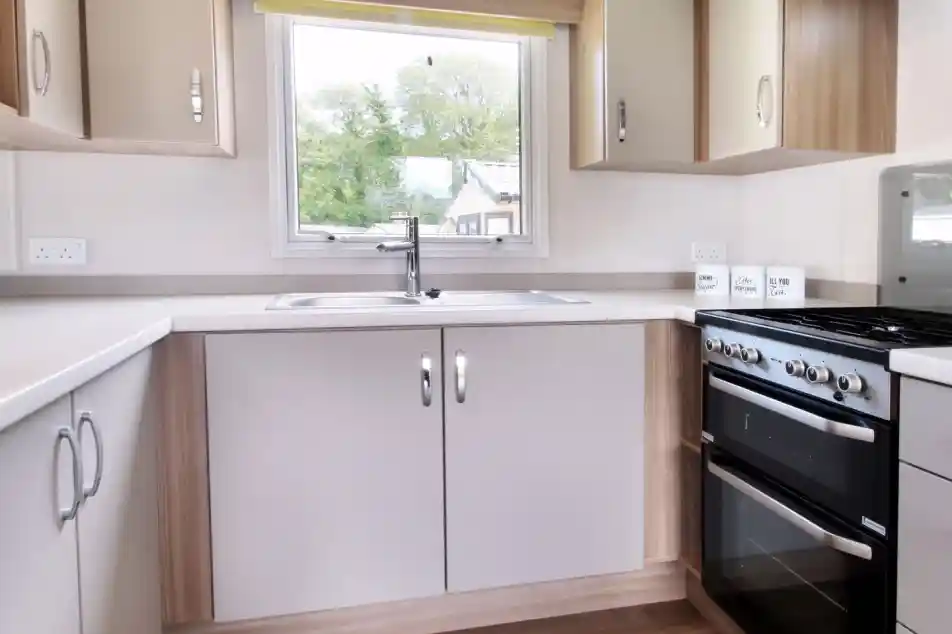 A modern kitchen featuring light-colored cabinets, a stainless steel sink, a four-burner gas stove, and a large window with a yellow blind, allowing natural light to enter.