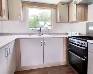 A modern kitchen featuring light-colored cabinets, a stainless steel sink, a four-burner gas stove, and a large window with a yellow blind, allowing natural light to enter.