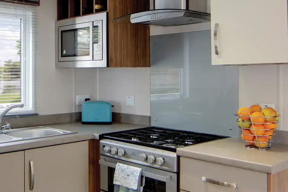 A modern kitchen counter with a stainless steel gas stove, a blue toaster, a microwave, and a basket of oranges.