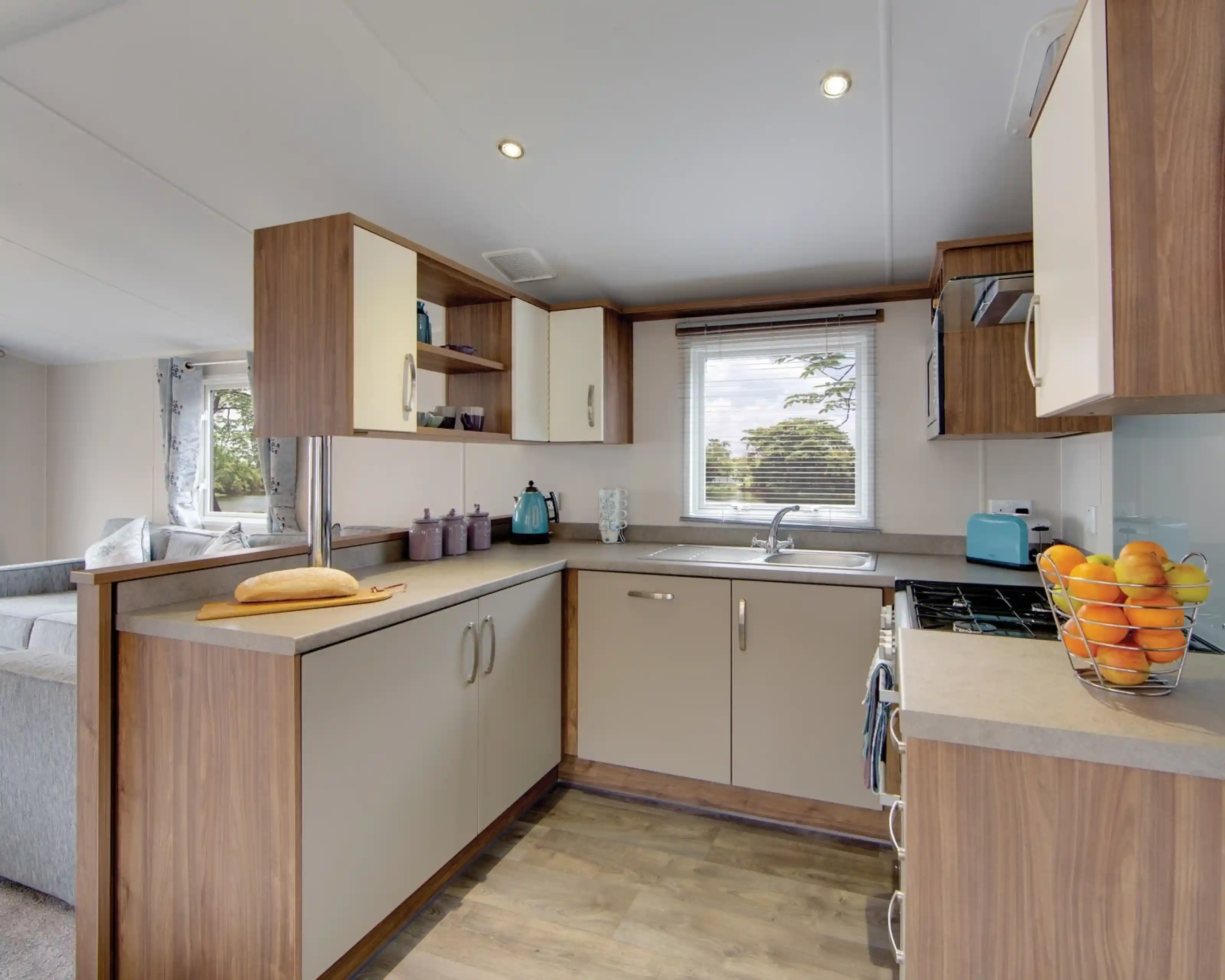 Modern kitchen with light wood cabinetry, a breakfast bar with bread, and a window overlooking trees.