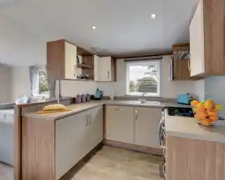 Modern kitchen with light wood cabinetry, a breakfast bar with bread, and a window overlooking trees.