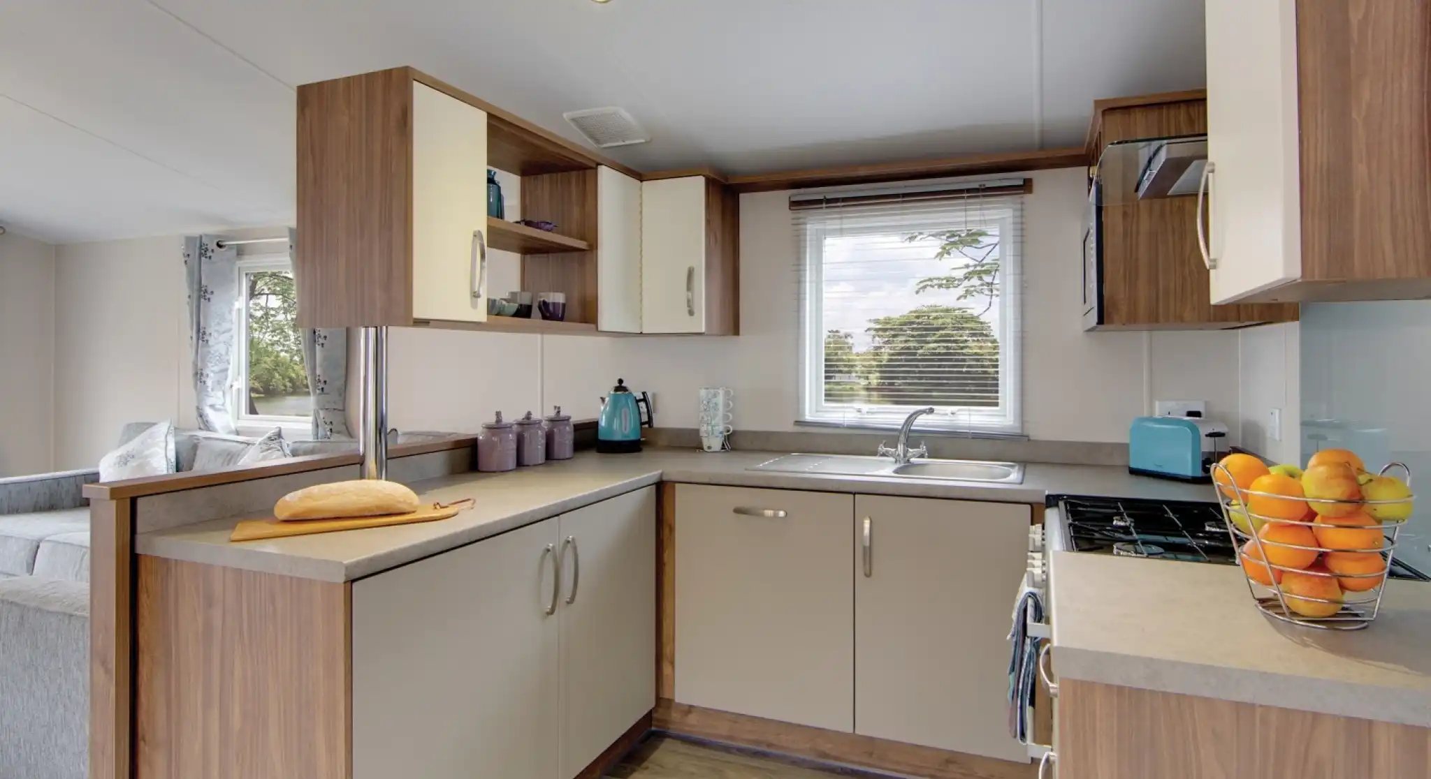 Modern kitchen with light wood cabinetry, a breakfast bar with bread, and a window overlooking trees.