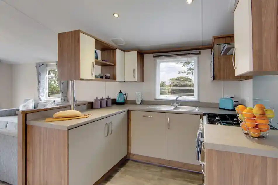 Modern kitchen with light wood cabinetry, a breakfast bar with bread, and a window overlooking trees.