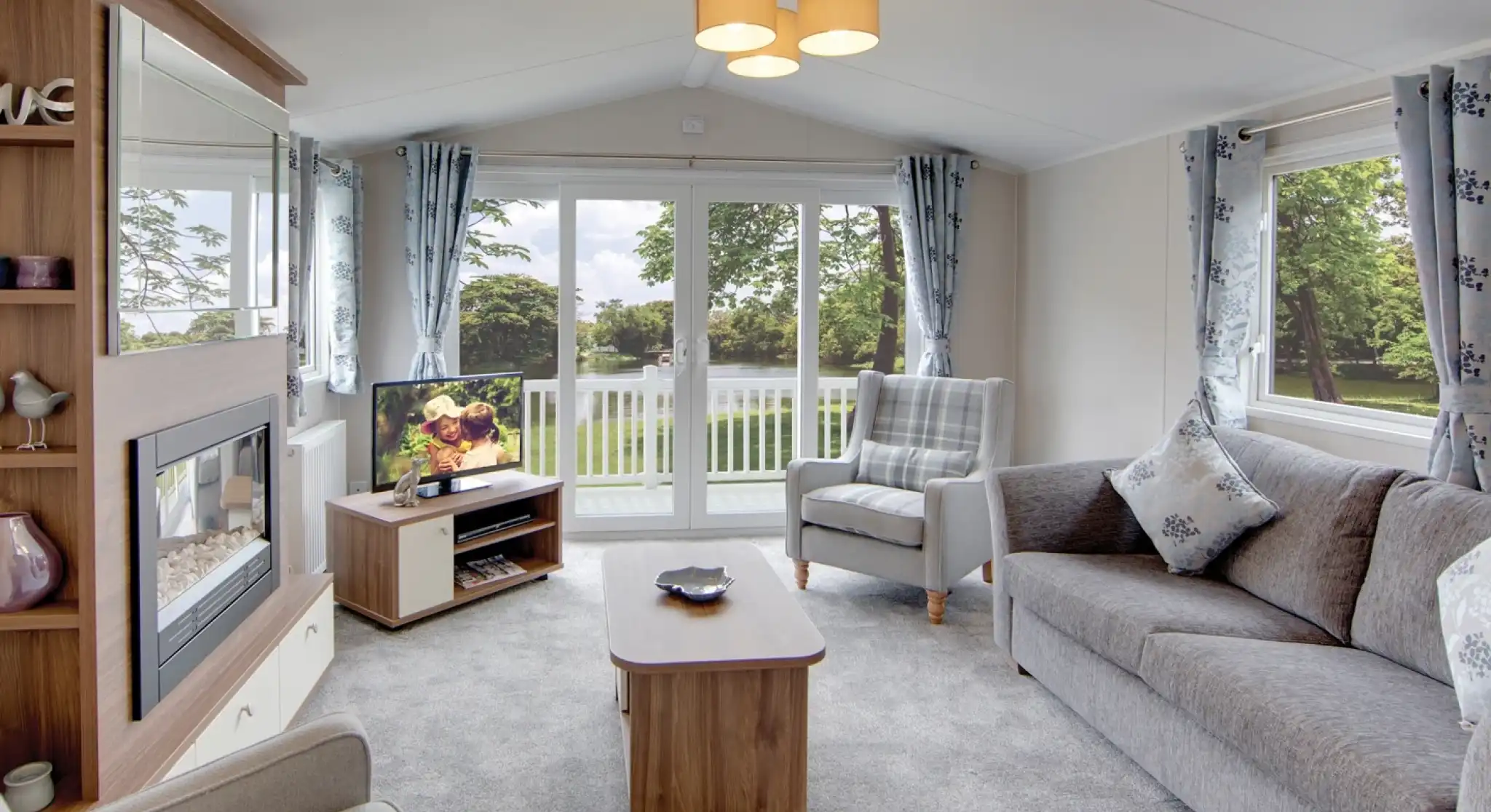 Modern living room with grey sofa, armchair, fireplace, and large sliding patio doors overlooking the decking.