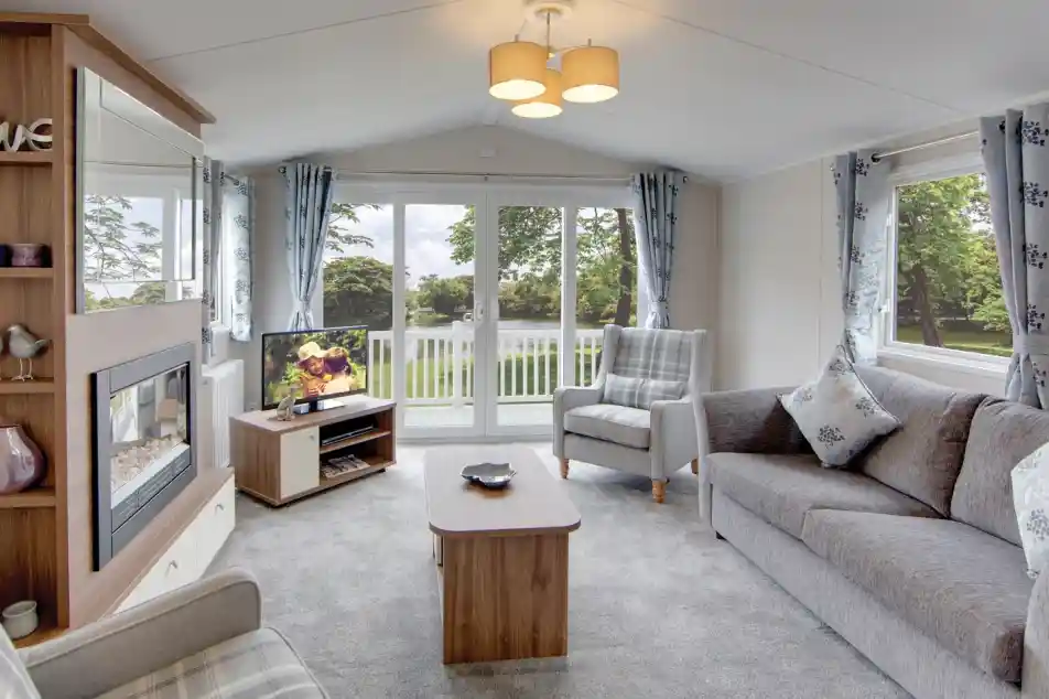 Modern living room with grey sofa, armchair, fireplace, and large sliding patio doors overlooking the decking.