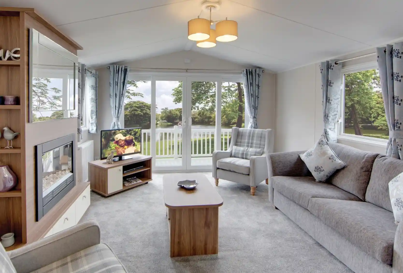 Modern living room with grey sofa, armchair, fireplace, and large sliding patio doors overlooking the decking.