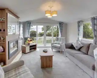 Modern living room with grey sofa, armchair, fireplace, and large sliding patio doors overlooking the decking.