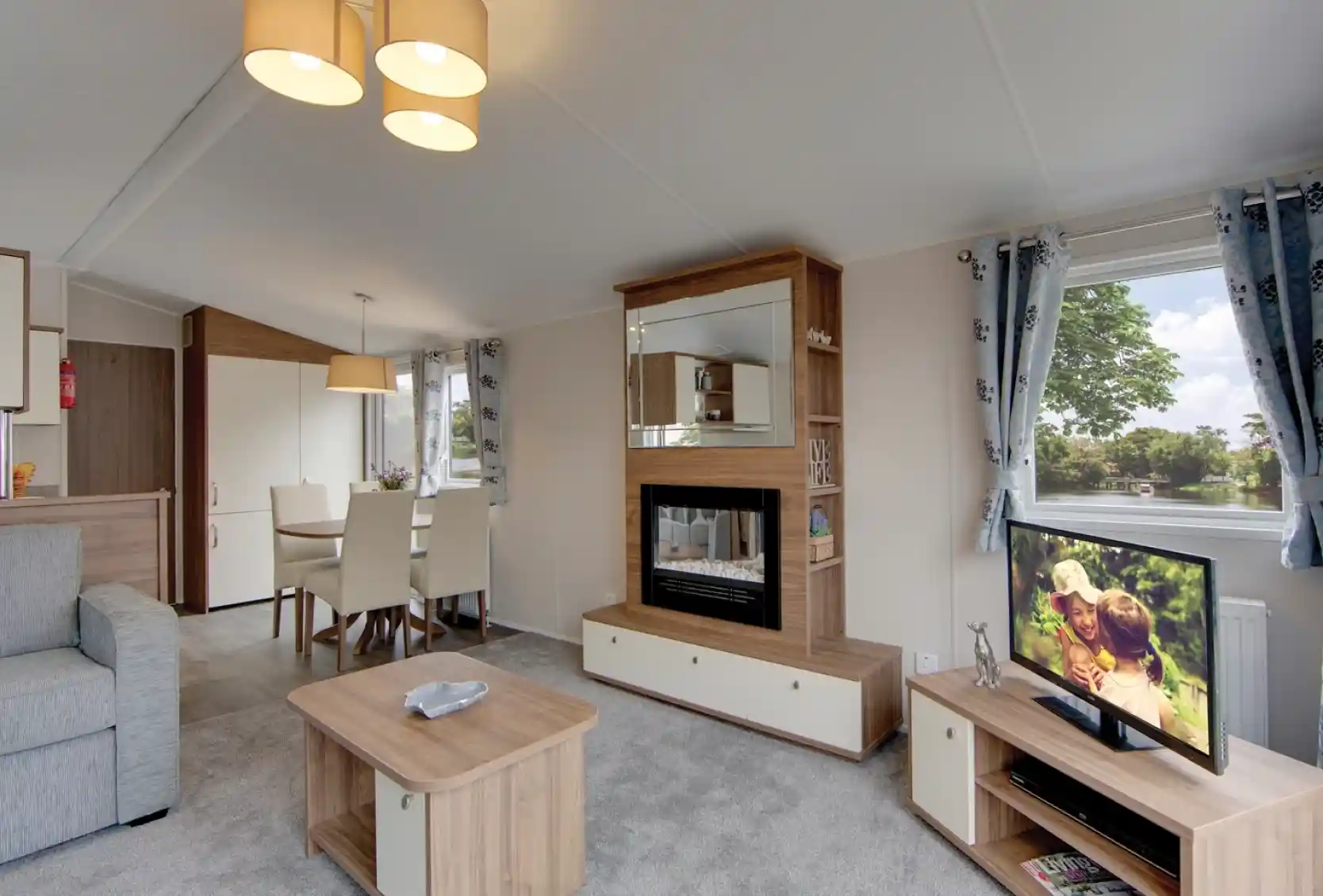 A modern living room with a fireplace, television, dining area, and sofa, featuring a scenic view from the window.