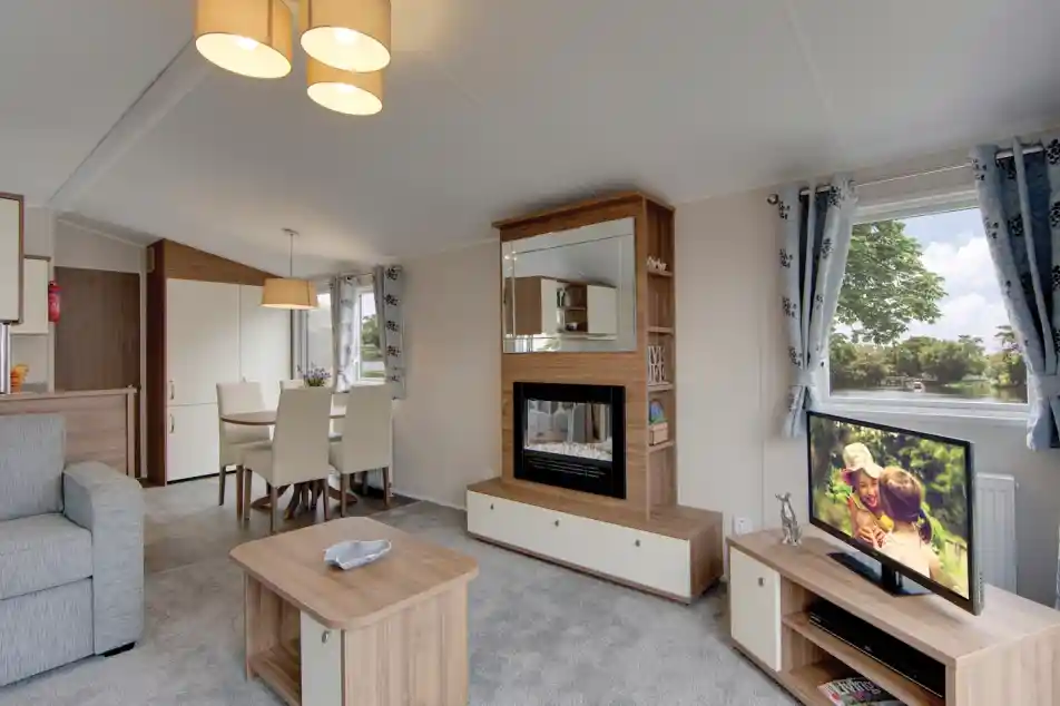 A modern living room with a fireplace, television, dining area, and sofa, featuring a scenic view from the window.