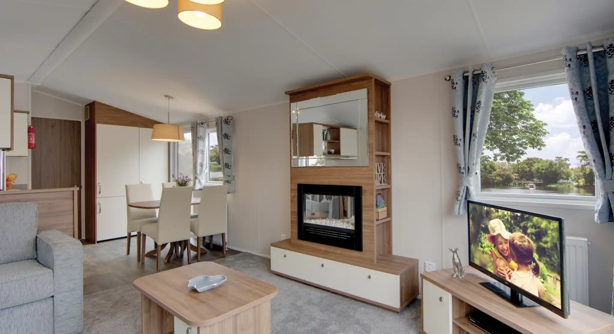 A modern living room with a fireplace, television, dining area, and sofa, featuring a scenic view from the window.