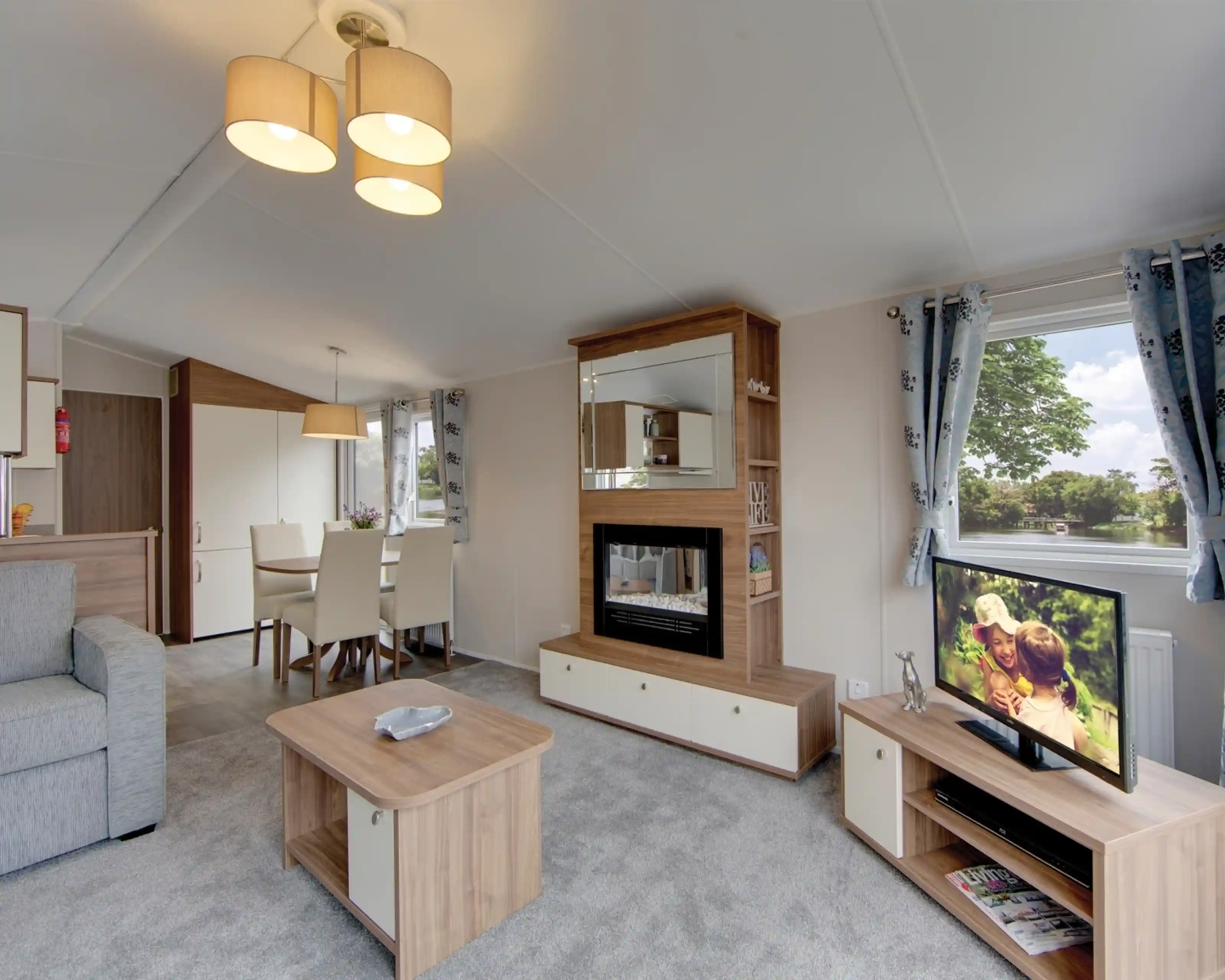 A modern living room with a fireplace, television, dining area, and sofa, featuring a scenic view from the window.