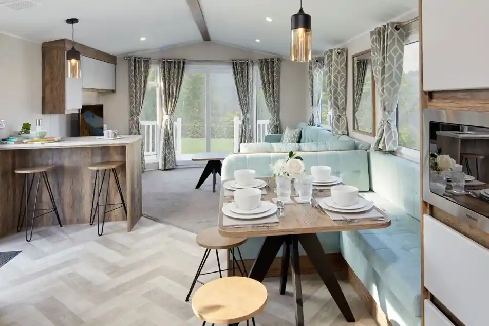 A bright and airy open plan sitting, dining room featuring a comfortable couch and a kitchen area with a breakfast bar and cabinetry. The space is adorned with furniture such as chairs and a dining room table, along with home appliances.