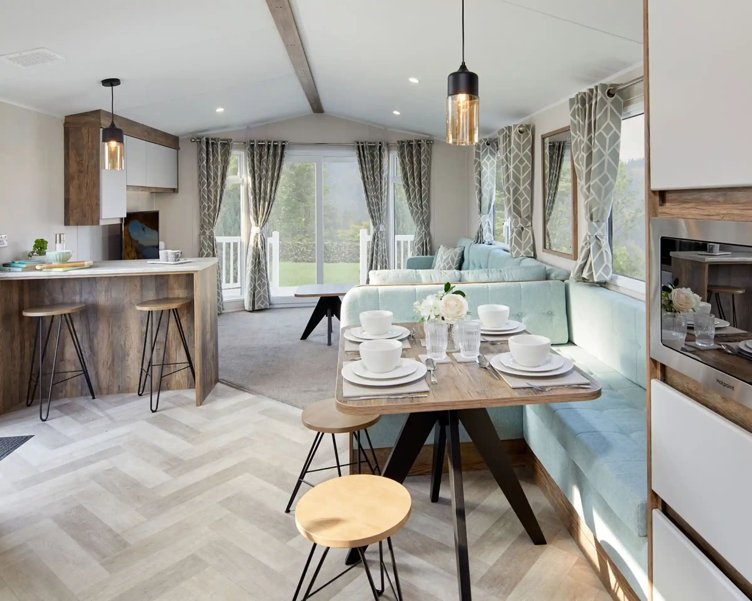 A bright and airy open plan sitting, dining room featuring a comfortable couch and a kitchen area with a breakfast bar and cabinetry. The space is adorned with furniture such as chairs and a dining room table, along with home appliances.