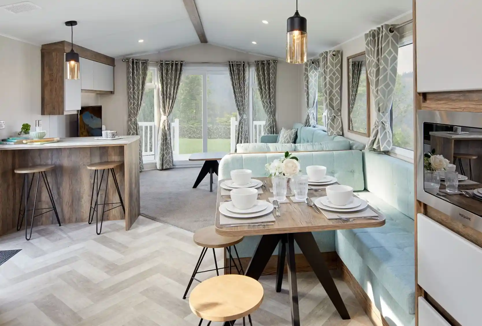 A bright and airy open plan sitting, dining room featuring a comfortable couch and a kitchen area with a breakfast bar and cabinetry. The space is adorned with furniture such as chairs and a dining room table, along with home appliances.