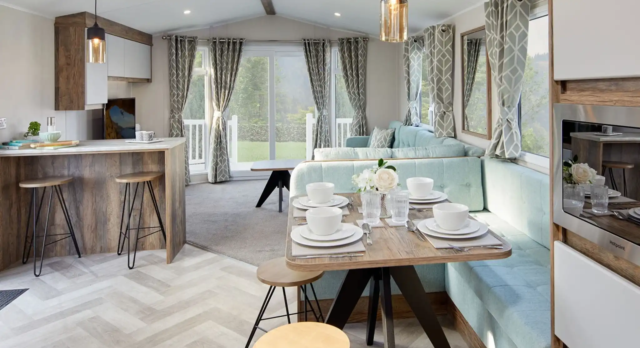 A bright and airy open plan sitting, dining room featuring a comfortable couch and a kitchen area with a breakfast bar and cabinetry. The space is adorned with furniture such as chairs and a dining room table, along with home appliances.