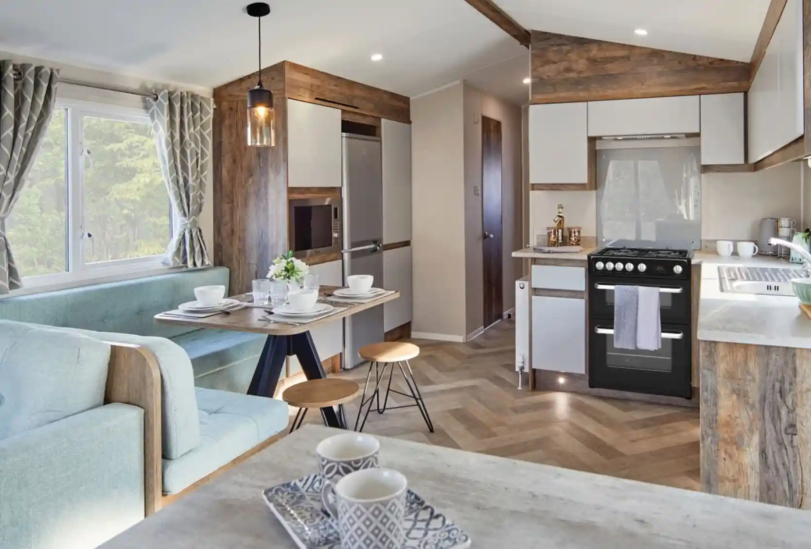 A spacious kitchen and dining room area featuring a comfortable couch and a table, with modern cabinetry, countertops, and home appliances. The space includes hardwood laminate flooring and is designed with an open floor plan.