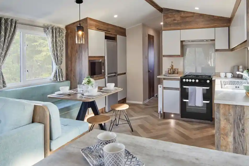 A spacious kitchen and dining room area featuring a comfortable couch and a table, with modern cabinetry, countertops, and home appliances. The space includes hardwood laminate flooring and is designed with an open floor plan.