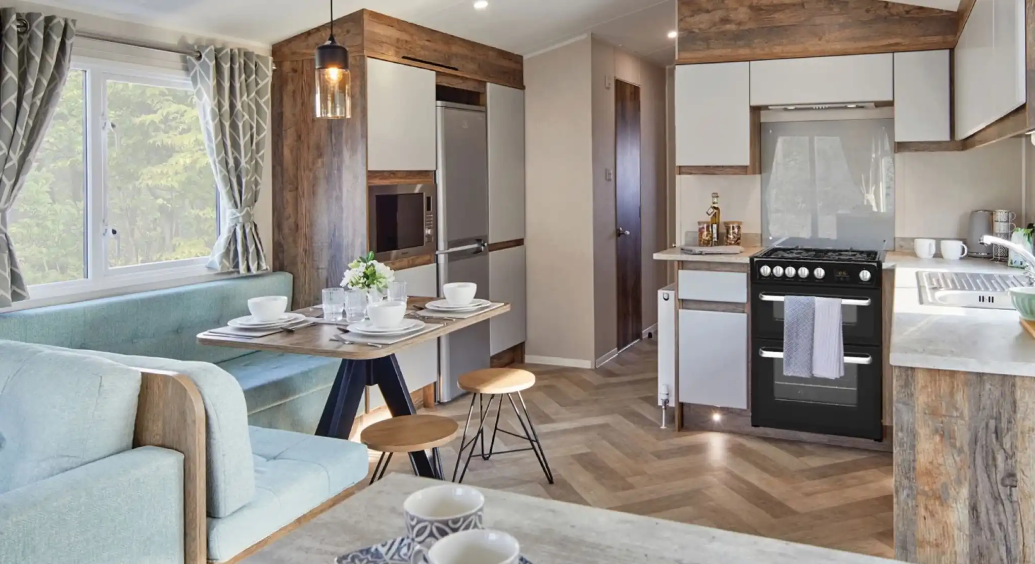 A spacious kitchen and dining room area featuring a comfortable couch and a table, with modern cabinetry, countertops, and home appliances. The space includes hardwood laminate flooring and is designed with an open floor plan.