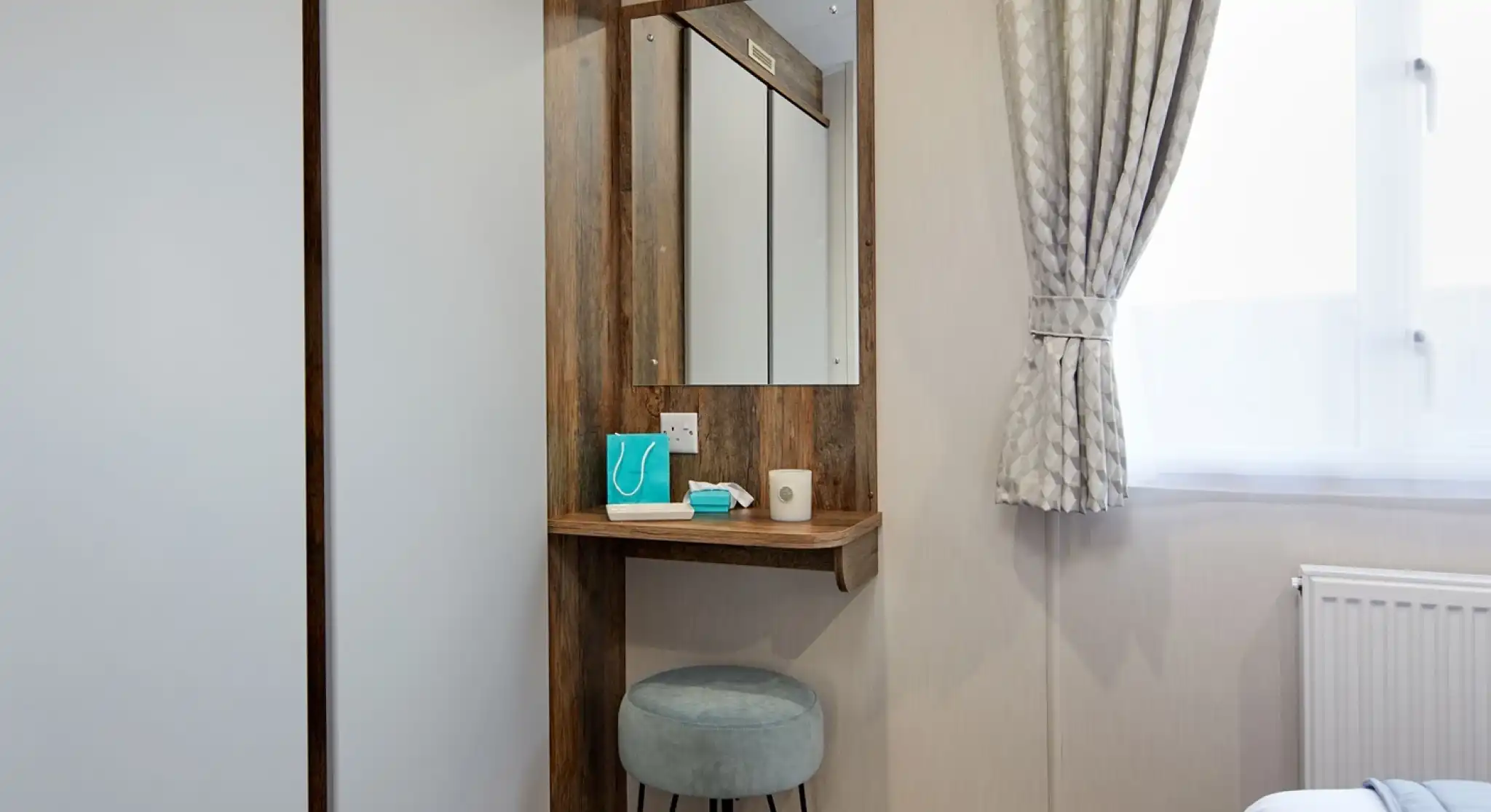 A room featuring a mirror on the wall with built-in small shelf table below  and double wardrobe.