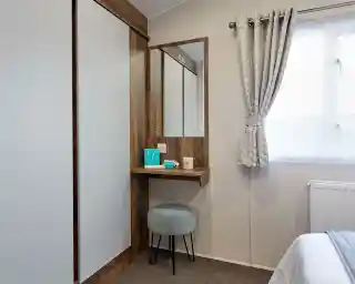 A room featuring a mirror on the wall with built-in small shelf table below  and double wardrobe.
