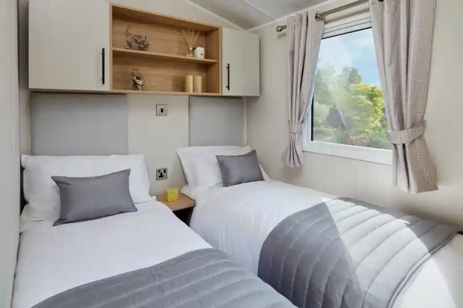 A bedroom with twin beds with crisp white sheets and pillows, together with headboards, overhead storage and a window.