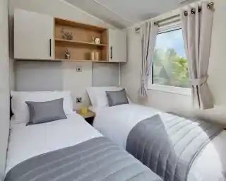 A bedroom with twin beds with crisp white sheets and pillows, together with headboards, overhead storage and a window.