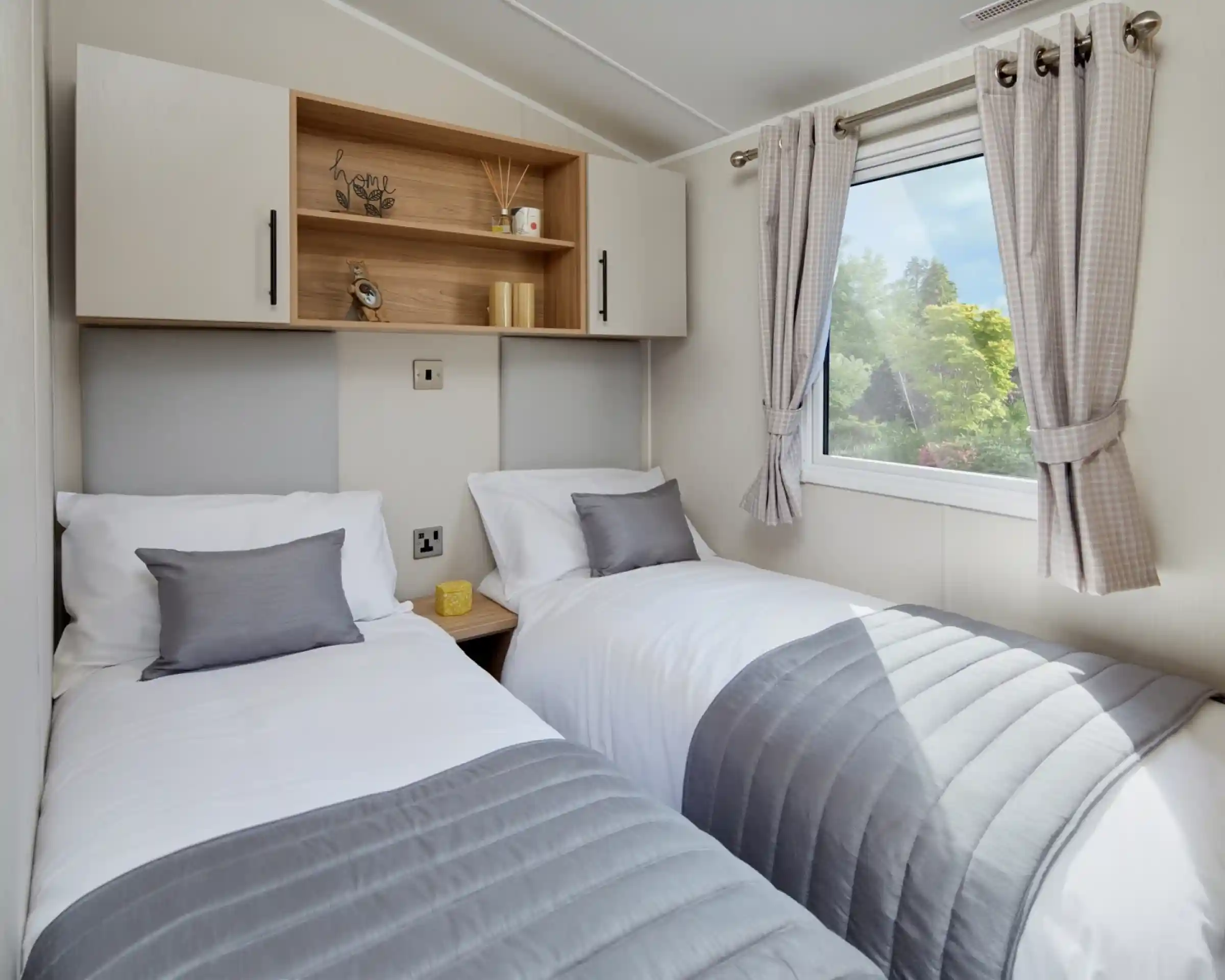 A bedroom with twin beds with crisp white sheets and pillows, together with headboards, overhead storage and a window.