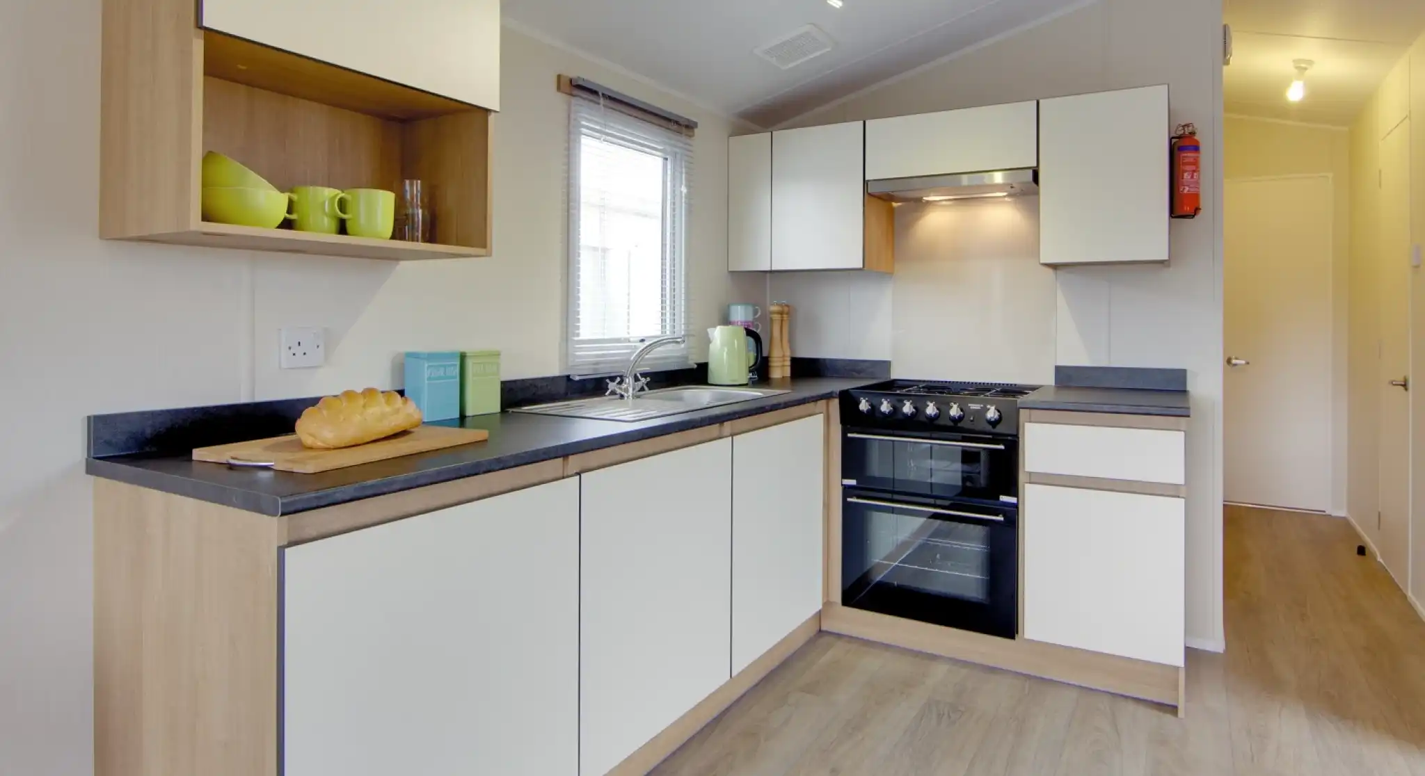 Modern kitchen with white cabinets, wood accents, stainless steel appliances, and a loaf of bread on the counter.