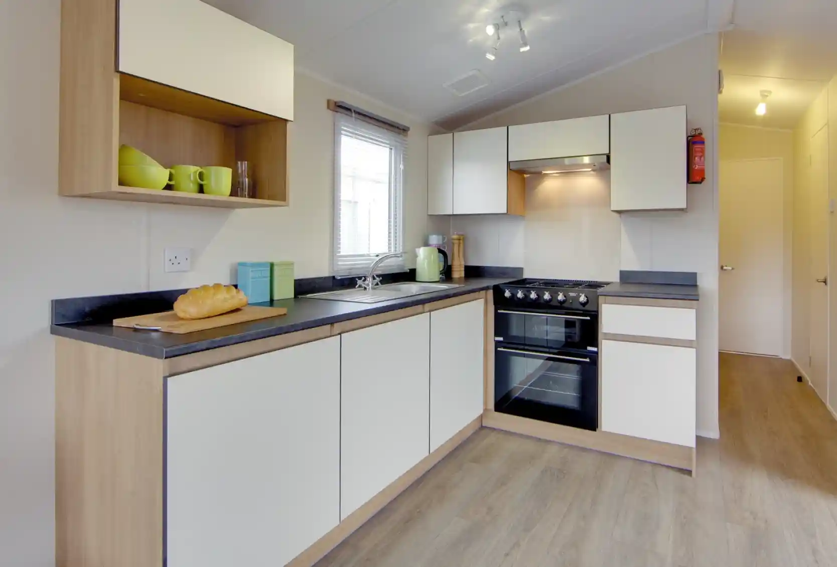 Modern kitchen with white cabinets, wood accents, stainless steel appliances, and a loaf of bread on the counter.