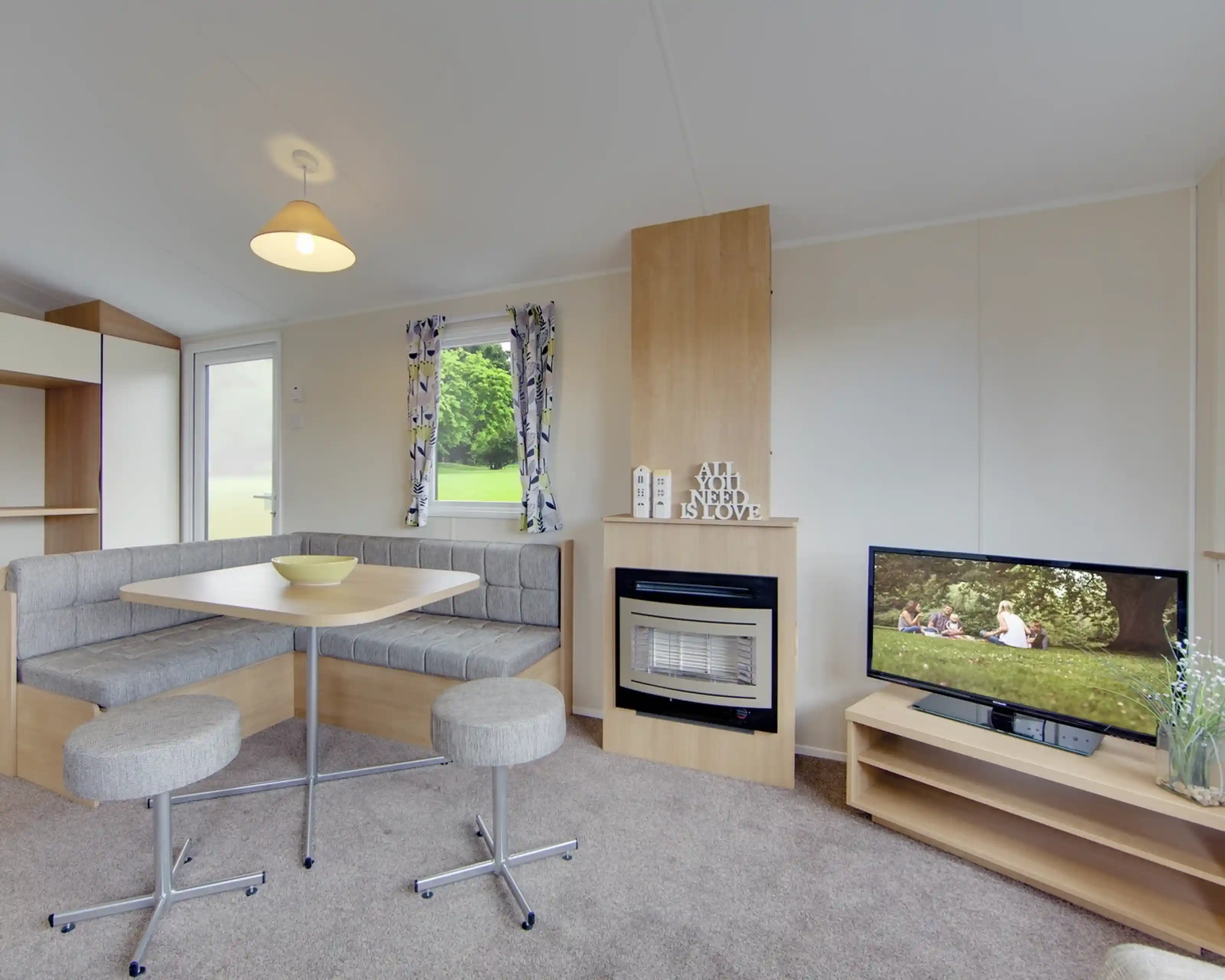 A caravan lounge with a dining banquette, fireplace, and television displaying a family picnic scene.