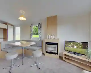 A caravan lounge with a dining banquette, fireplace, and television displaying a family picnic scene.