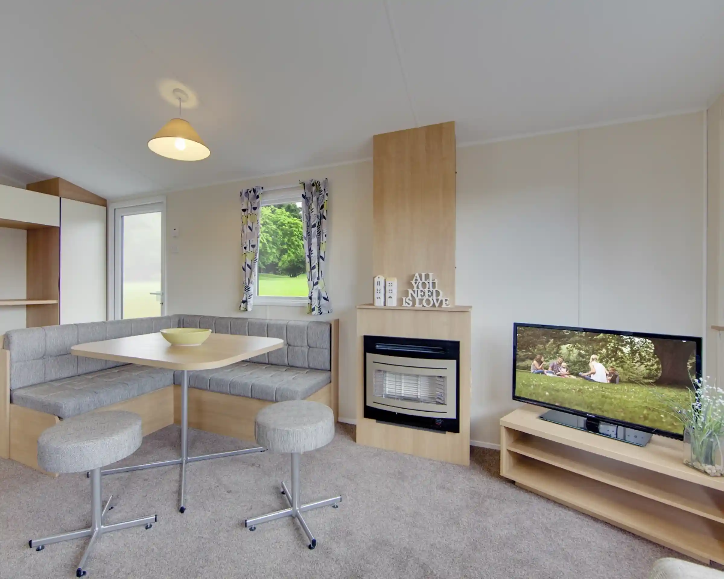 A caravan lounge with a dining banquette, fireplace, and television displaying a family picnic scene.