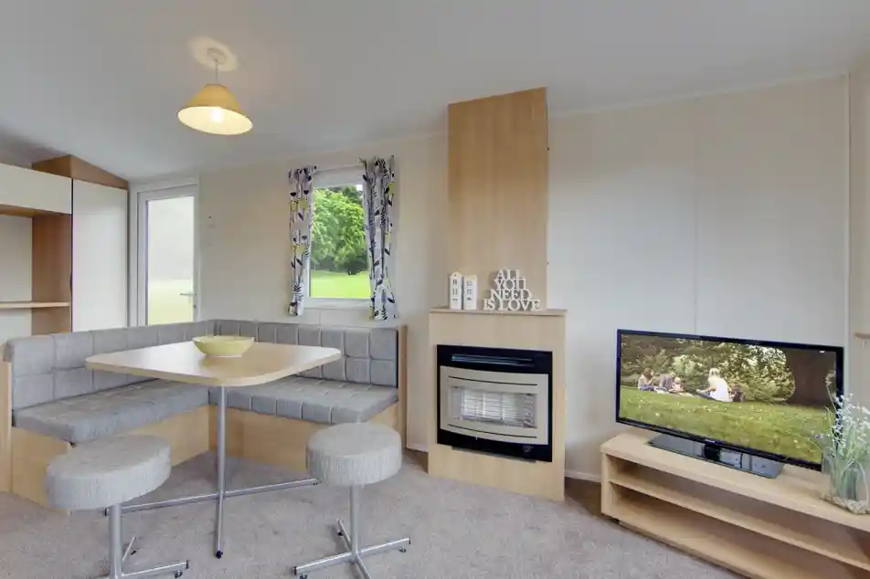 A caravan lounge with a dining banquette, fireplace, and television displaying a family picnic scene.