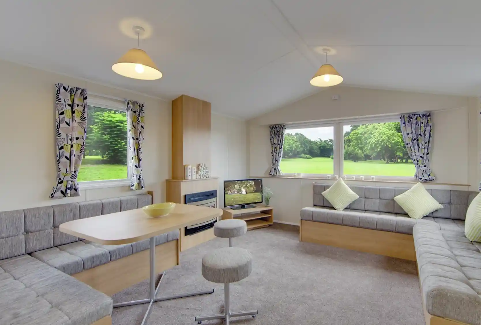 Modern living area with L-shaped sofa, dining table, and large windows overlooking a green landscape.