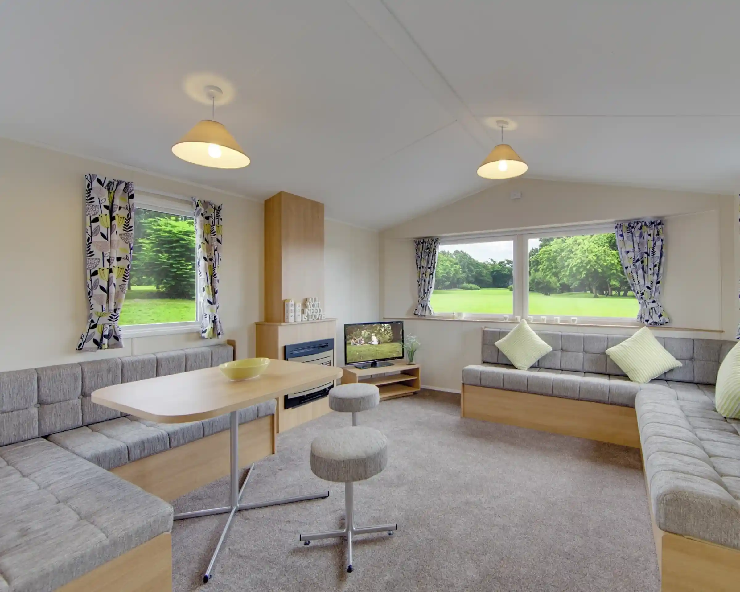 Modern living area with L-shaped sofa, dining table, and large windows overlooking a green landscape.