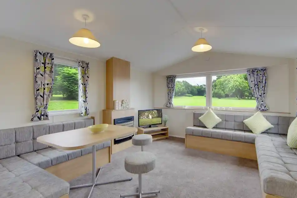 Modern living area with L-shaped sofa, dining table, and large windows overlooking a green landscape.