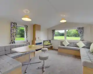 Modern living area with L-shaped sofa, dining table, and large windows overlooking a green landscape.