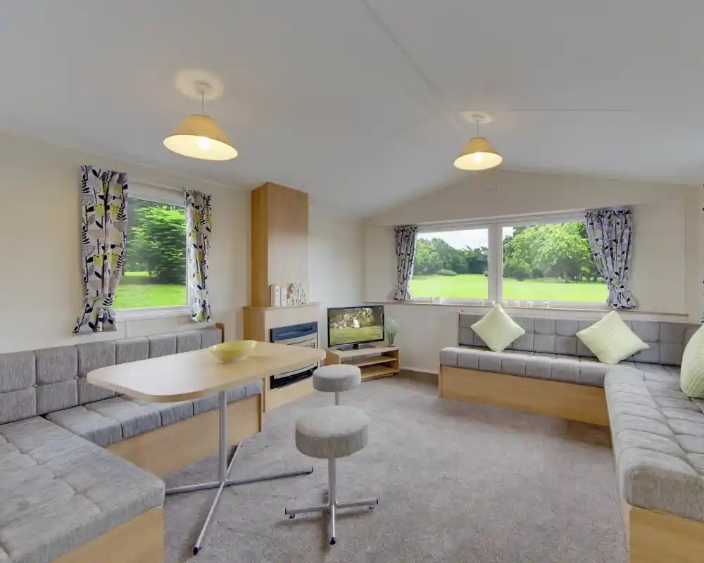 Modern living area with L-shaped sofa, dining table, and large windows overlooking a green landscape.