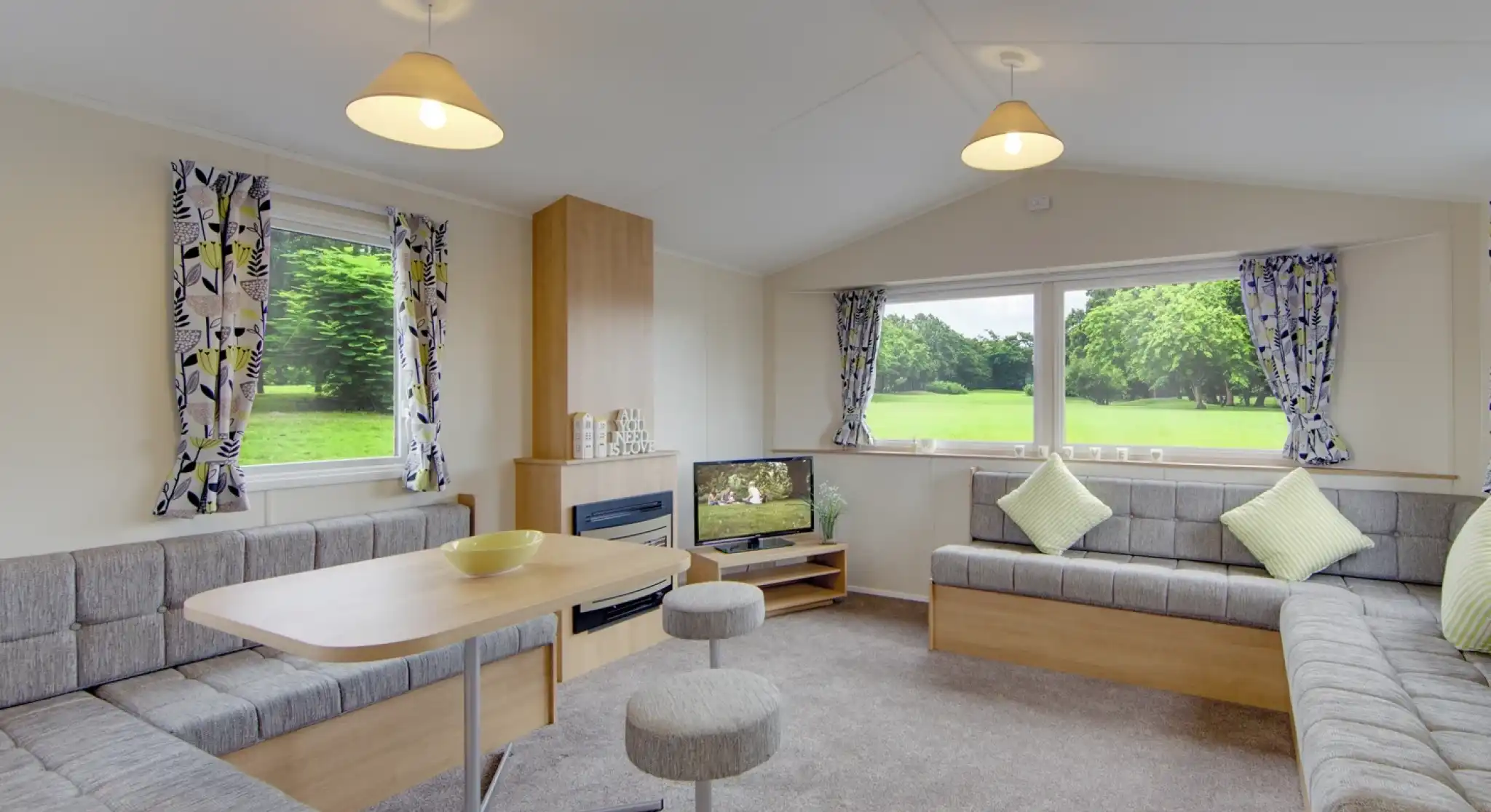 Modern living area with L-shaped sofa, dining table, and large windows overlooking a green landscape.