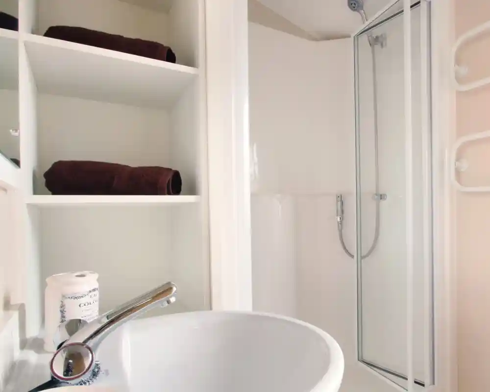 A shower room with enclosed shower, wash basin and shelving.
