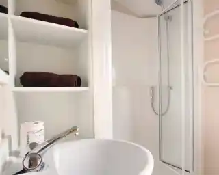 A shower room with enclosed shower, wash basin and shelving.