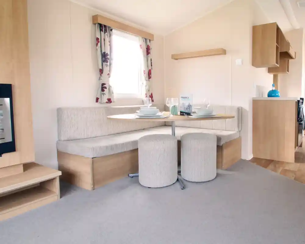 A dining area with L-shaped built-in corner cushioned seating and two stools with oval dining table.