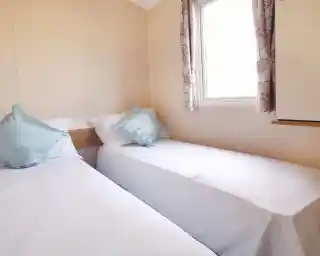 A twin bedroom with twin single beds and crisp white sheets and a window with floral curtains.