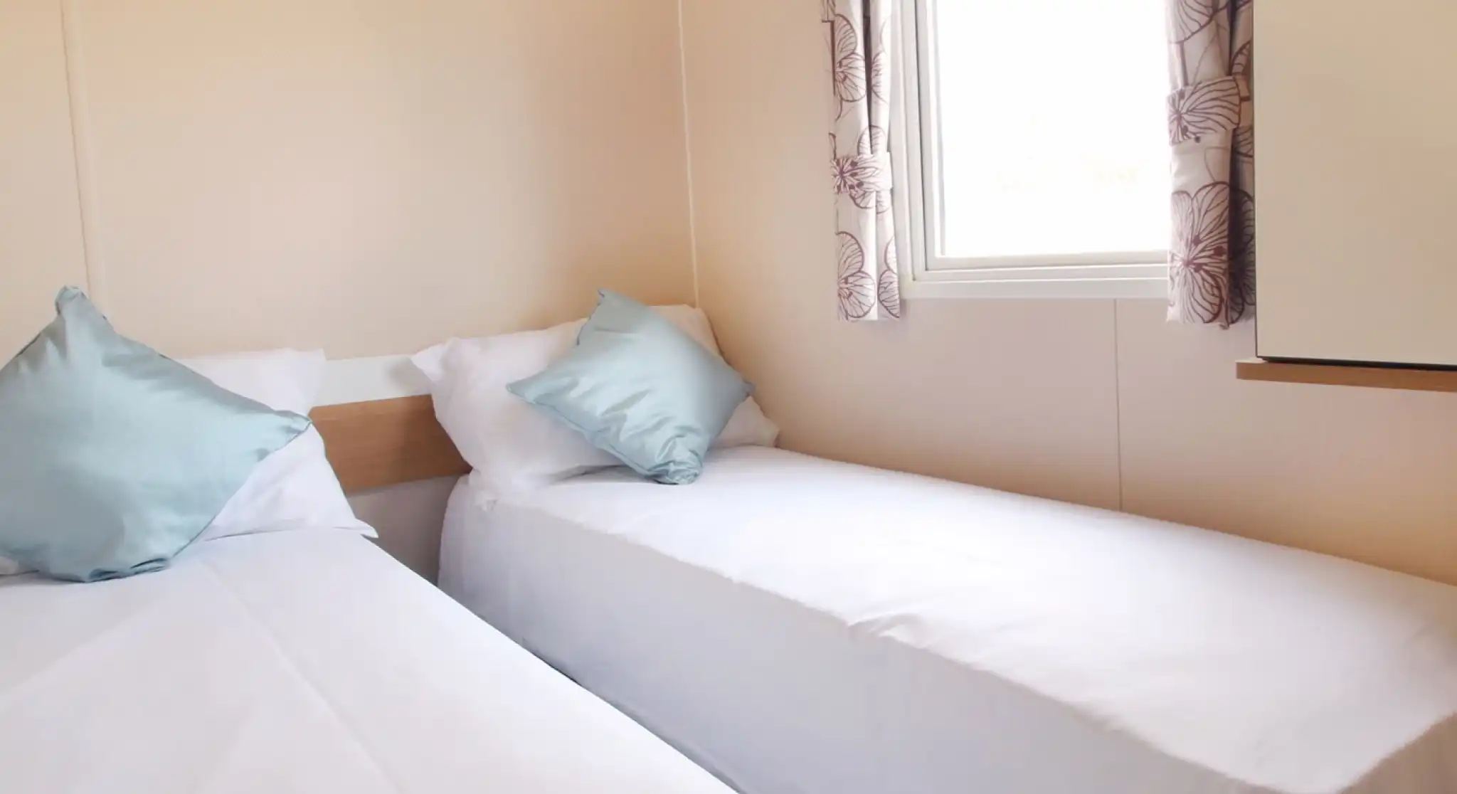 A twin bedroom with twin single beds and crisp white sheets and a window with floral curtains.