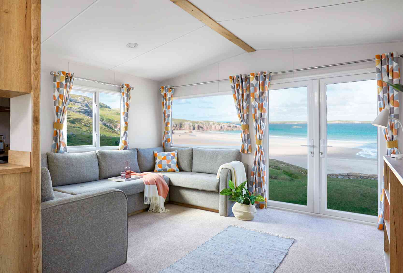 A bright living room with a couch, coffee table, and a window that offers a scenic beach view.