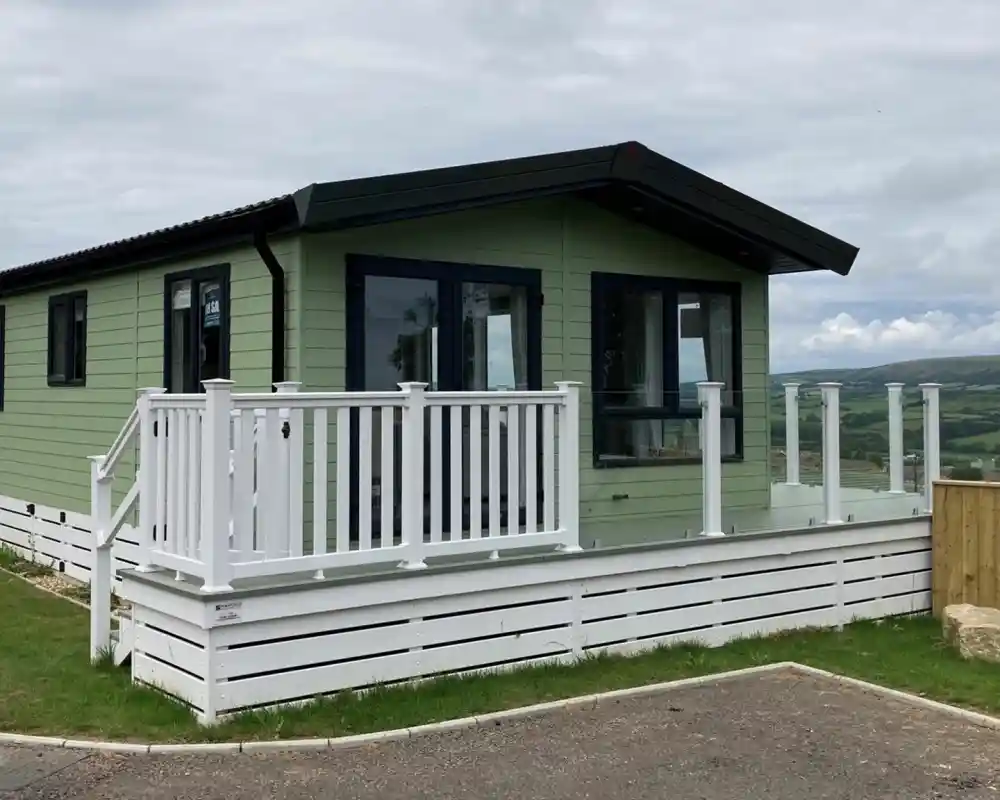 Exterior of the Atlas Lilac Lodge at Swanage Coastal Park with decking and glass balustrade to make the most of the views.