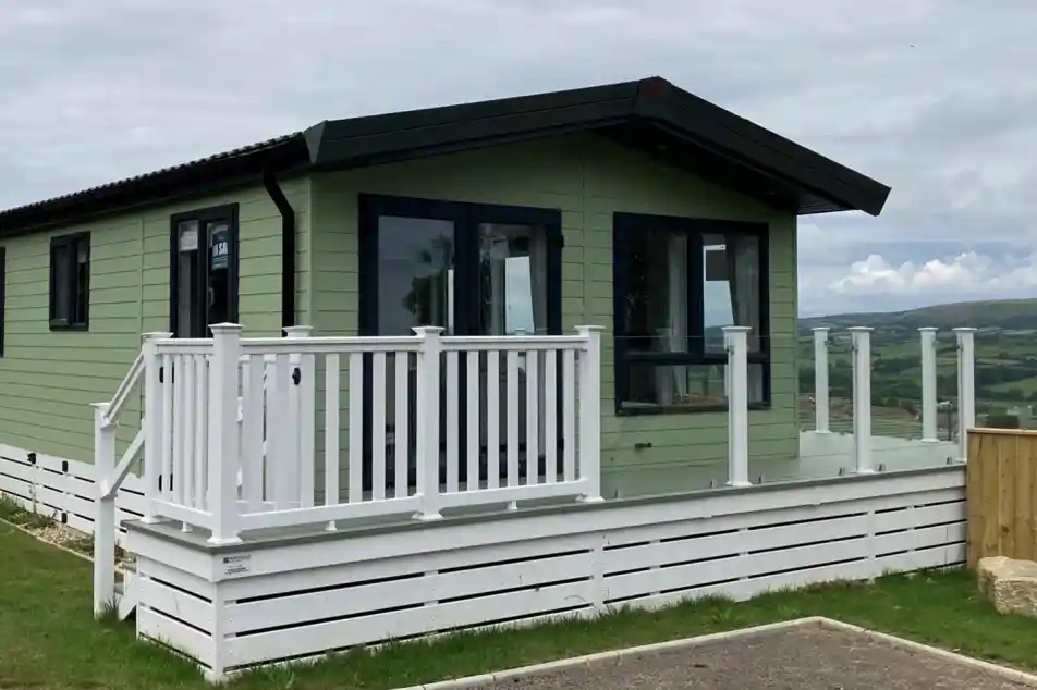Exterior of the Atlas Lilac Lodge at Swanage Coastal Park with decking and glass balustrade to make the most of the views.