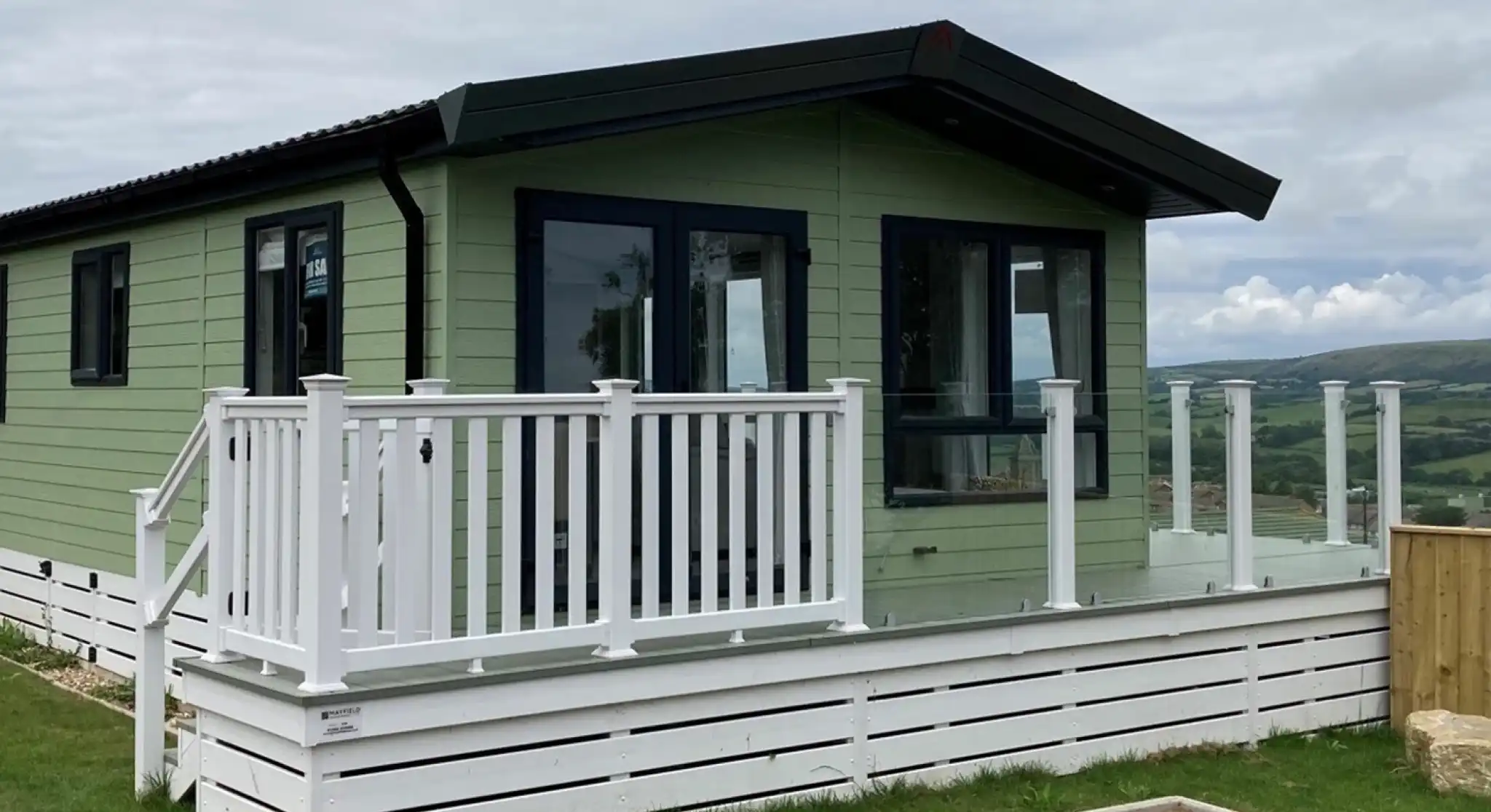 Exterior of the Atlas Lilac Lodge at Swanage Coastal Park with decking and glass balustrade to make the most of the views.